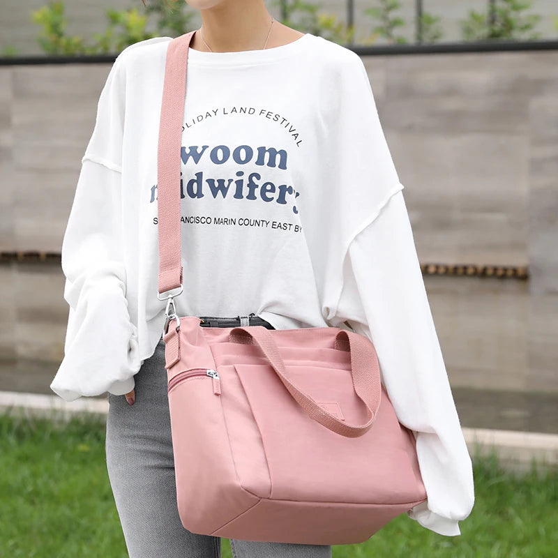 A person is holding a pink nylon tote bag with a zipper closure against a blurred outdoor background.