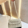 A hand holds a silver rhinestone evening clutch bag against a textured light background.