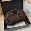 Un pochette à clochette en fibre naturelle brun foncé est présentée dans une boîte noire avec une carte blanche.