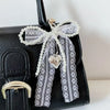 Black handbag featuring a white pearl bow keychain with a heart pendant
