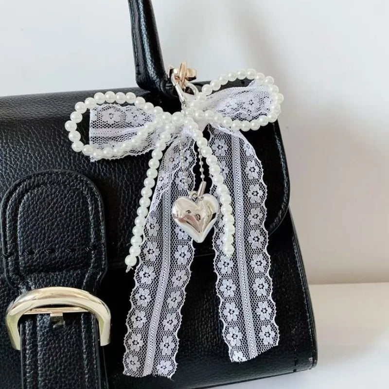 Black handbag featuring a white pearl bow keychain with a heart pendant