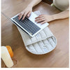 A person places a silver laptop into a beige embroidered cotton sleeve on a wooden table.