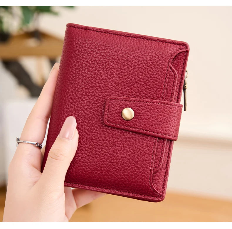 A hand holds a deep red textured card holder wallet with a leather flap and gold accent.