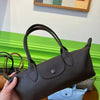 A brown storage shoulder bag is held by a hand, displayed against a white wall with a green stripe and other bags.