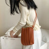 A woman is holding a brown PU leather pleated crossbody bag against a white background.