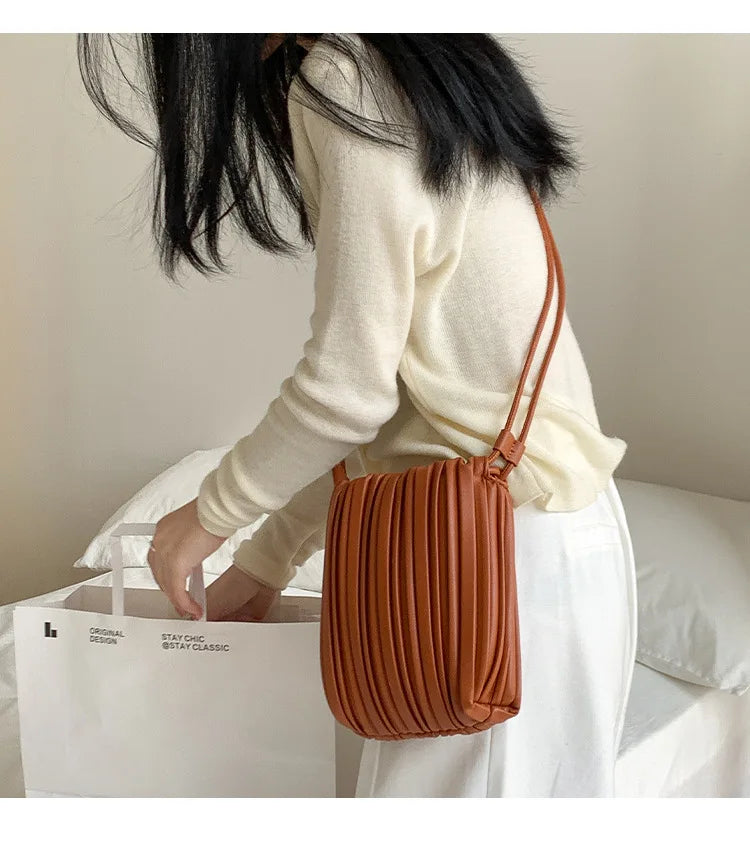 A woman is holding a brown PU leather pleated crossbody bag against a white background.