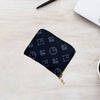 A dark blue patterned zippered card holder wallet resting on a light wooden surface next to a pen and a white notebook.