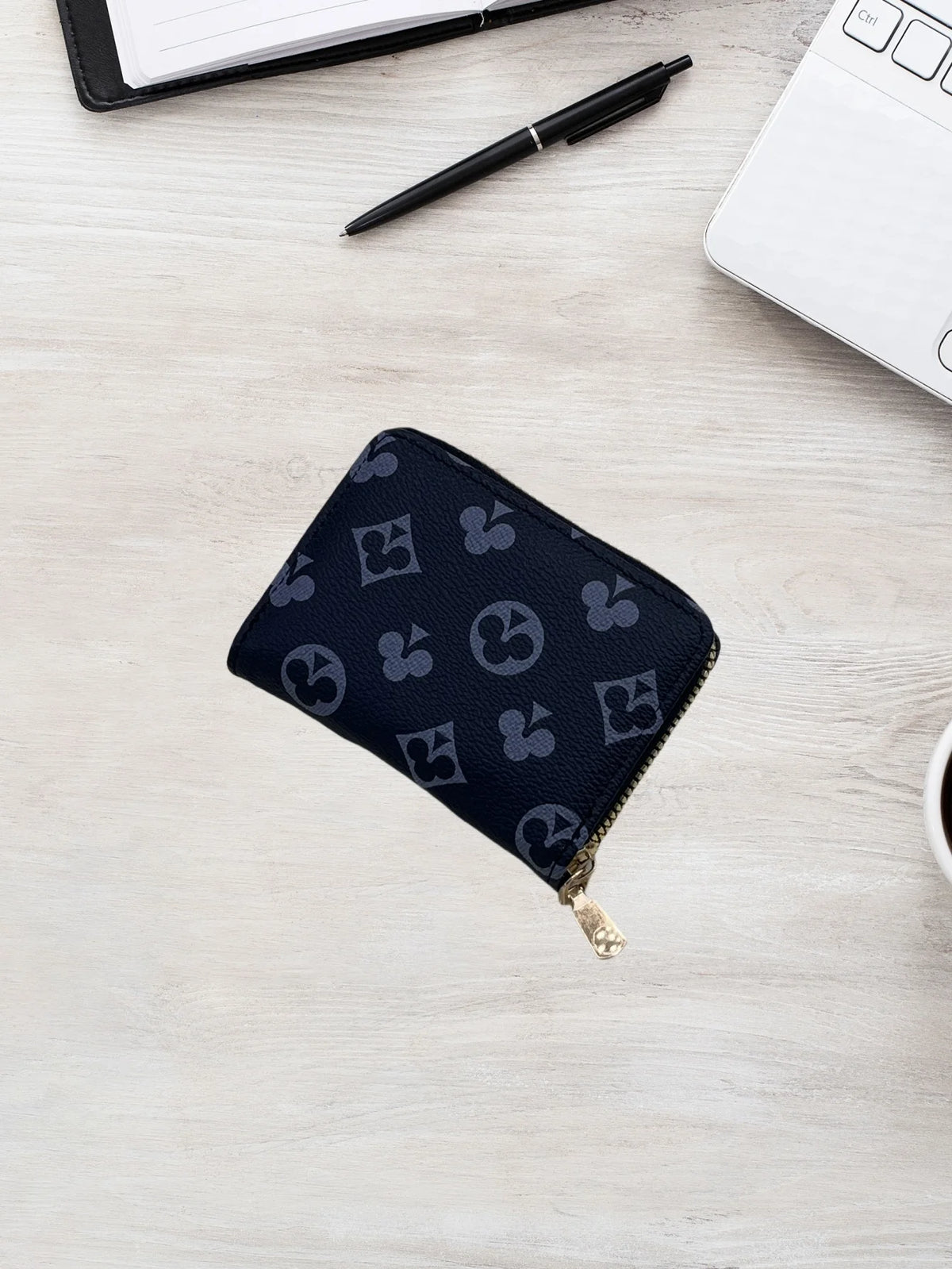A dark blue patterned zippered card holder wallet resting on a light wooden surface next to a pen and a white notebook.