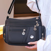 A black waterproof nylon crossbody tote bag with gold hardware being held by a person wearing a white shirt.