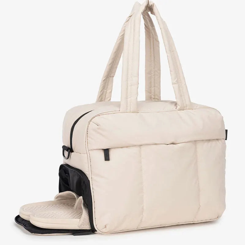 A beige large capacity women's travel duffle bag with padded handles and a zippered closure.