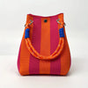 A retro knitted bucket handbag featuring vertical stripes of orange and magenta with blue trim.
