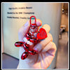 A hand holds a red balloon dog keychain charm with a heart pendant against a light background.
