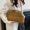 A woman holds a woven straw tote handbag in olive green against a white blazer.