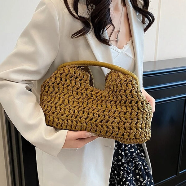 A woman holds a woven straw tote handbag in olive green against a white blazer.