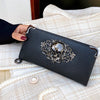 A black punk style long leather wallet resting on a cream textured fabric.