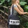 A woman wearing a grey top rests her hand on a wooden railing while holding a musical note tote bag with piano lace trim and 