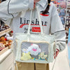 A person holds a transparent white shoulder tote bag with a pink and yellow cloud charm in a retail setting.