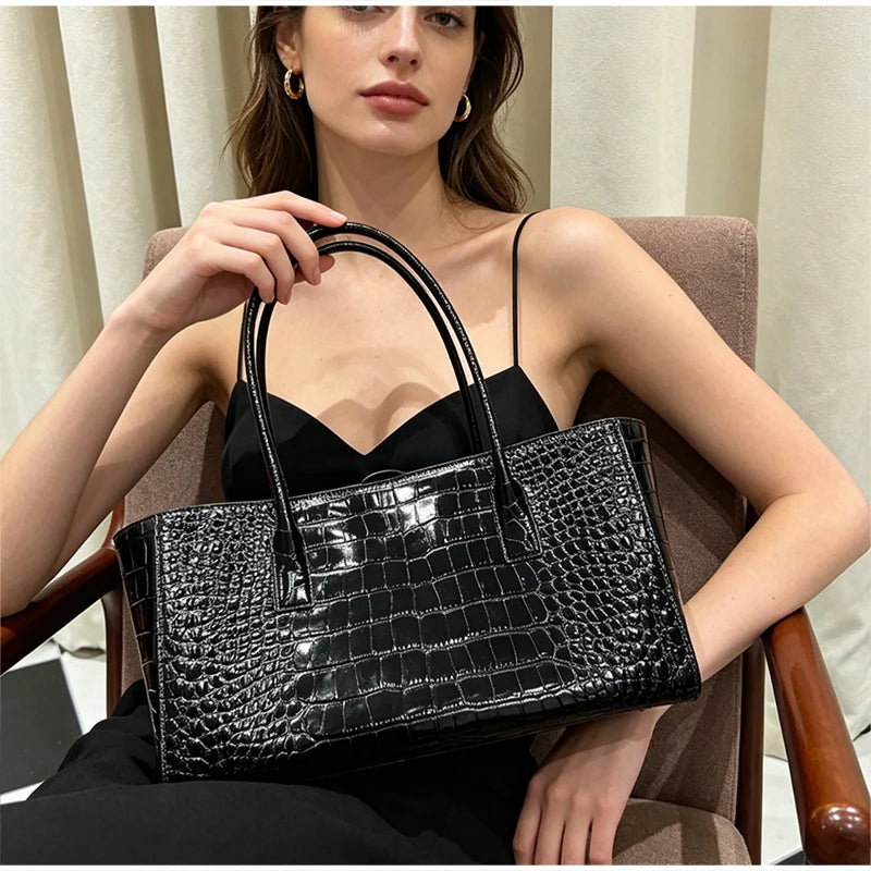 A woman holds a black crocodile embossed leather tote bag with a magnetic closure.