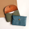 A stack of three genuine leather card holders or coin purses in shades of terracotta, olive green, and teal.