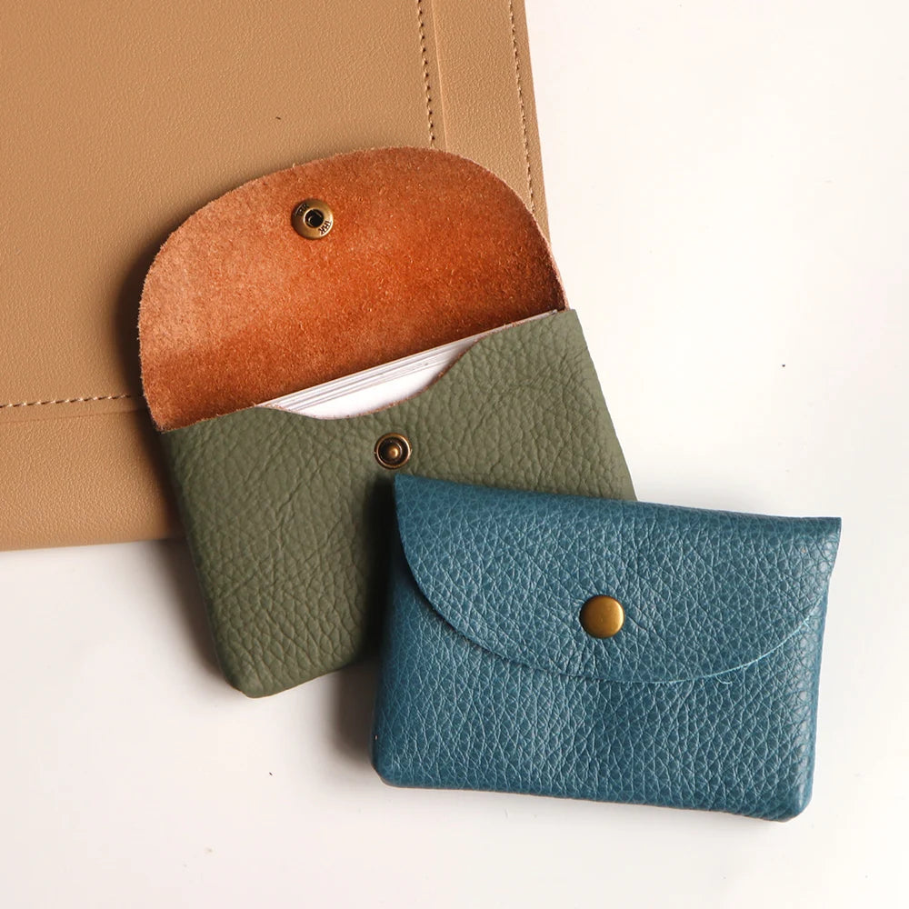 A stack of three genuine leather card holders or coin purses in shades of terracotta, olive green, and teal.