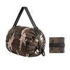 A camouflage patterned foldable nylon storage bag with a black handle and a matching fabric strap.