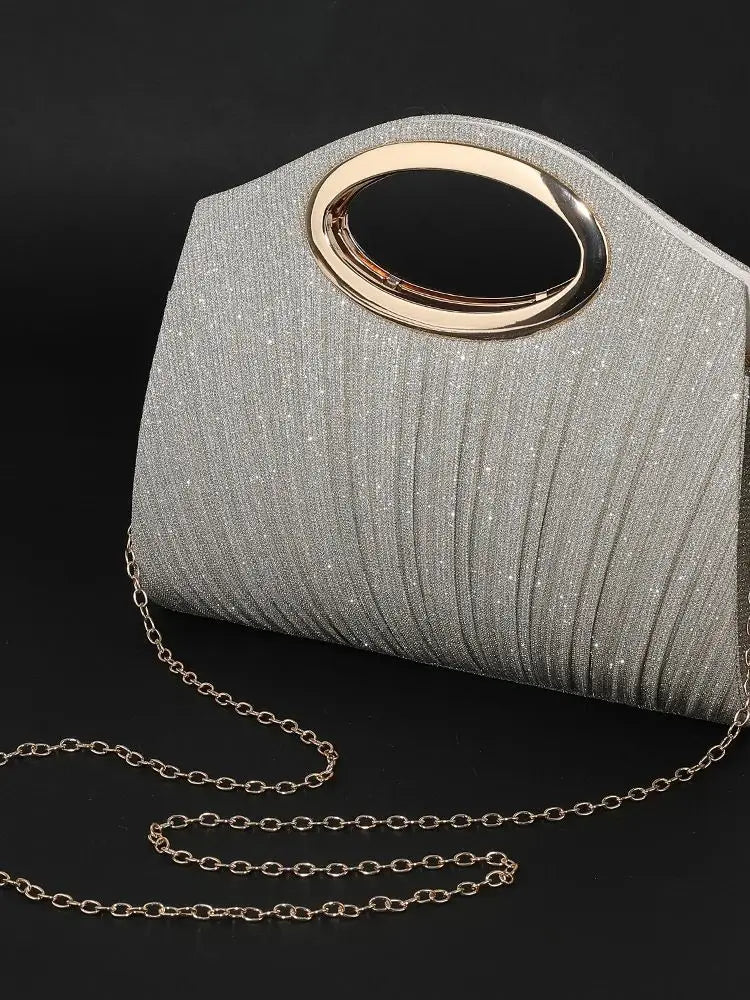 Silberglitzernde plissierte Handtasche mit goldfarbener runder Schnalle und Ketten auf schwarzem Hintergrund.