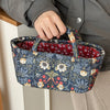 A hand holds a quilted fabric storage basket with blue floral embroidery against a gray jacket.