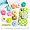 A collection of colorful, flower-shaped phone grips and a green checkered phone case are displayed on a white background.