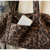 A close-up of a brown leopard print canvas tote bag showing a pocket with a striped cosmetic item.