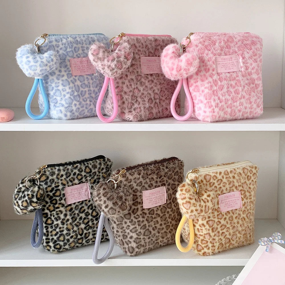 Three leopard print makeup bags with fuzzy handles and pink, blue, and beige tones displayed on a white shelf.