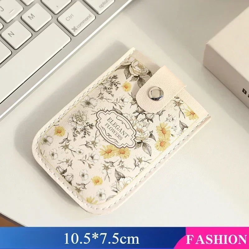 A beige floral patterned card wallet with a leather strap resting on a white surface.