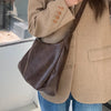 A person is holding a brown vintage PU leather tote bag with a long strap against a light colored jacket and blue jeans.