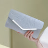 A hand holds a light gray glitter pleated crossbody clutch bag with a white trim against a pale background.