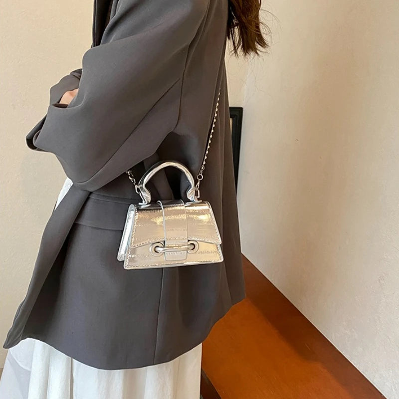 A gray blazer sleeve shows an elegant silver square crossbody bag with a chain strap.