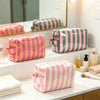 A collection of striped cosmetic bags in pink and green are displayed on a white counter.