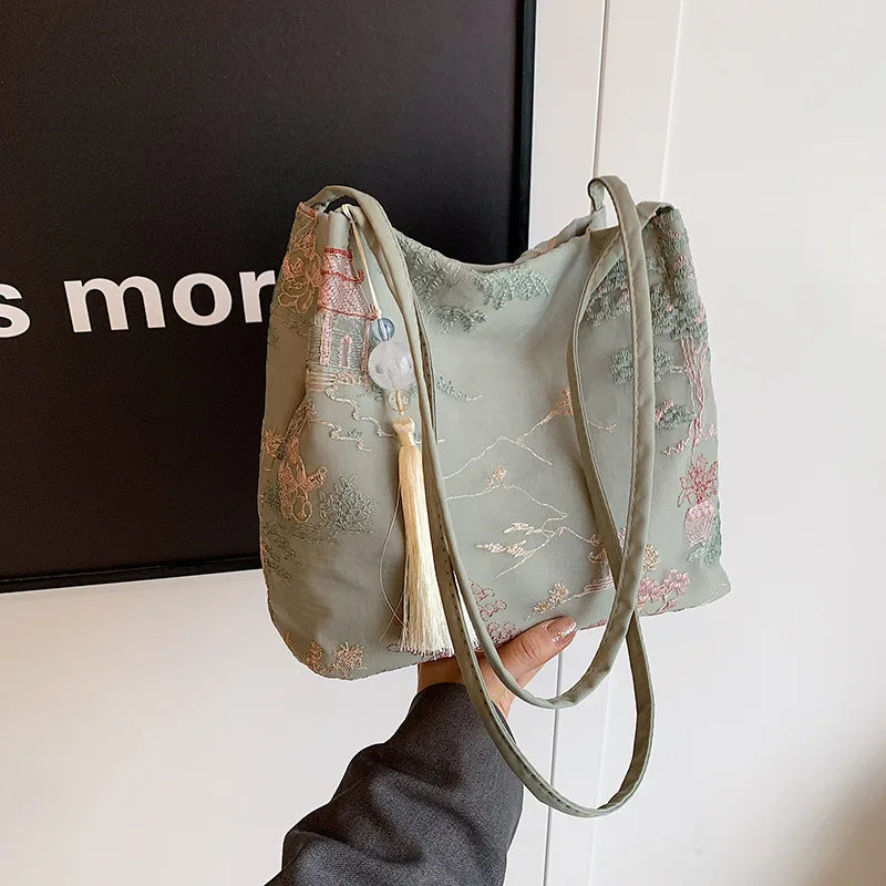 Bolso de seda jacquard verde salvia con bordado floral rosa que sostiene una persona.