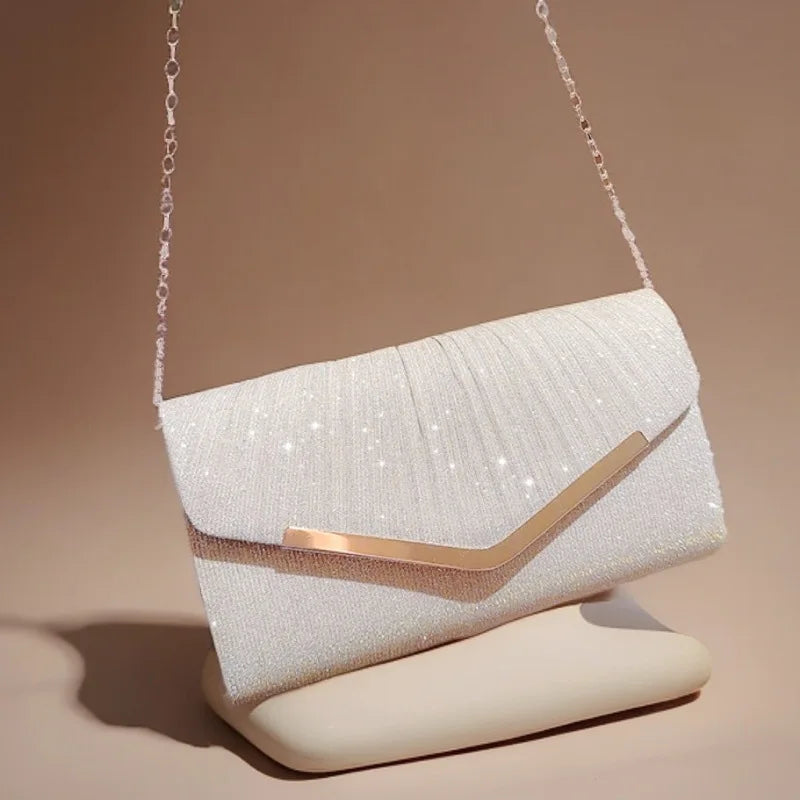 A white glitter pleated crossbody clutch bag with a gold accent, displayed on a light surface.