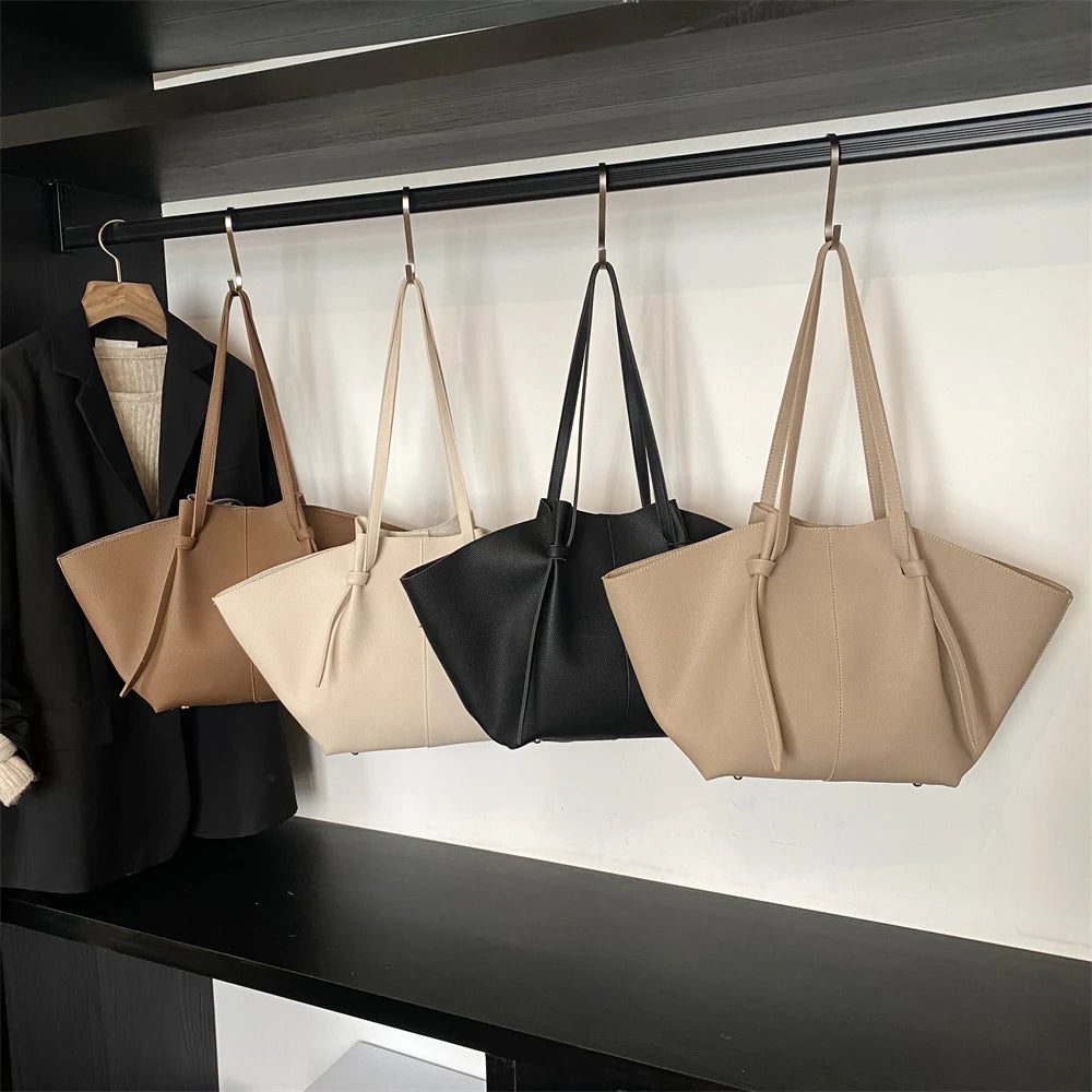 Four luxury PU leather shoulder tote bags in beige and black are hanging on a shelf.
