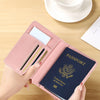 A hand holds a pink slim passport holder containing a blue passport and an ID card on a wooden table.