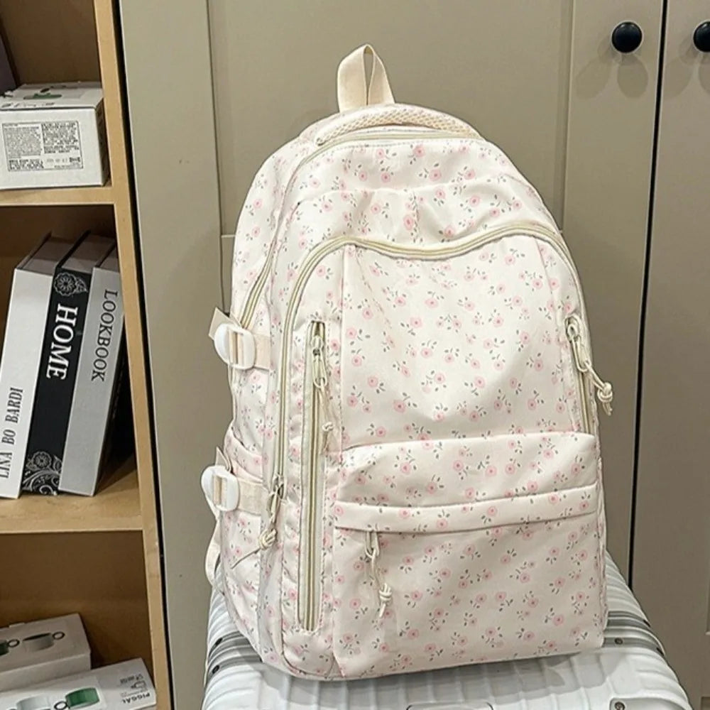 Una mochila de varios bolsillos con estampado floral rosa claro, exhibida en un estante.