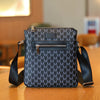 A dark gray men's lightweight crossbody sling bag with a zippered front pocket resting on a wooden surface.
