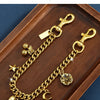 A gold-colored chain necklace with a charm featuring a cherry flower and a star, displayed in a wooden tray.