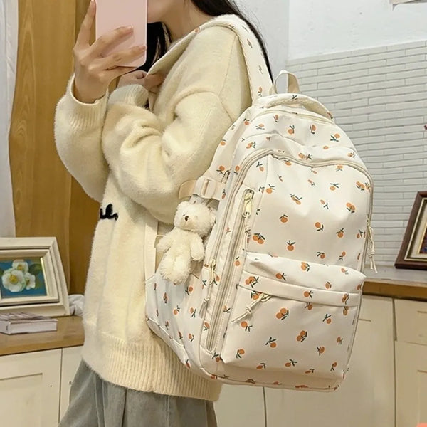 Una persona sostiene un suéter de punto de color crema y lleva una mochila con estampado floral y múltiples bolsillos.