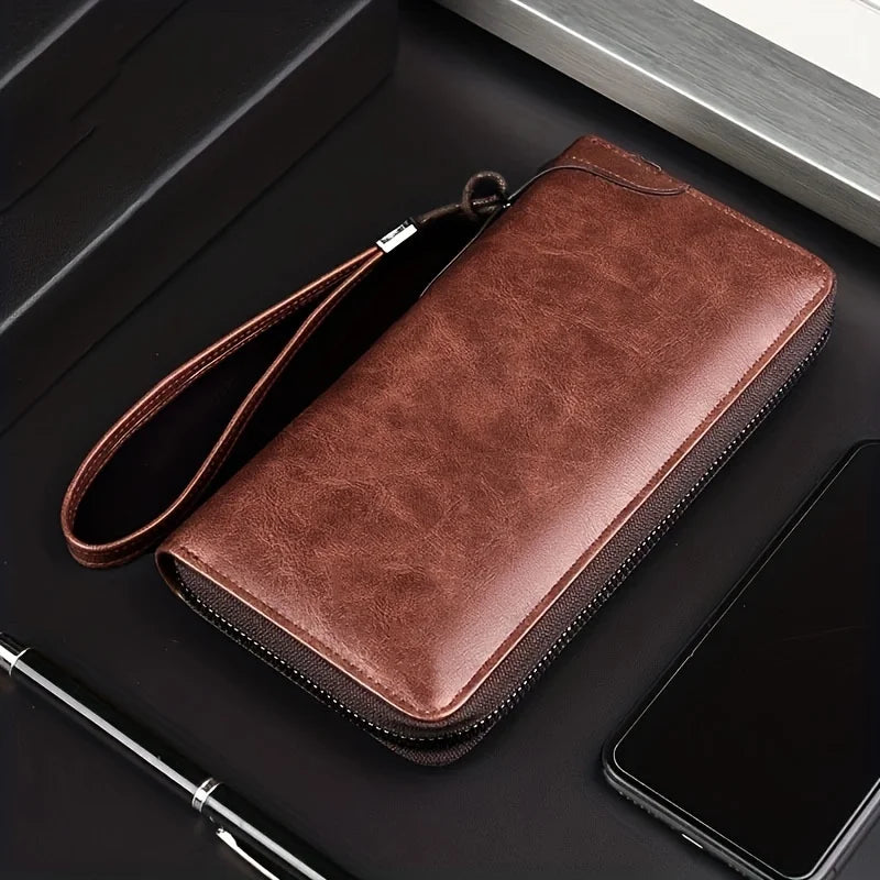 A brown men's PU leather zipper wallet resting on a dark surface next to a smartphone and pen.