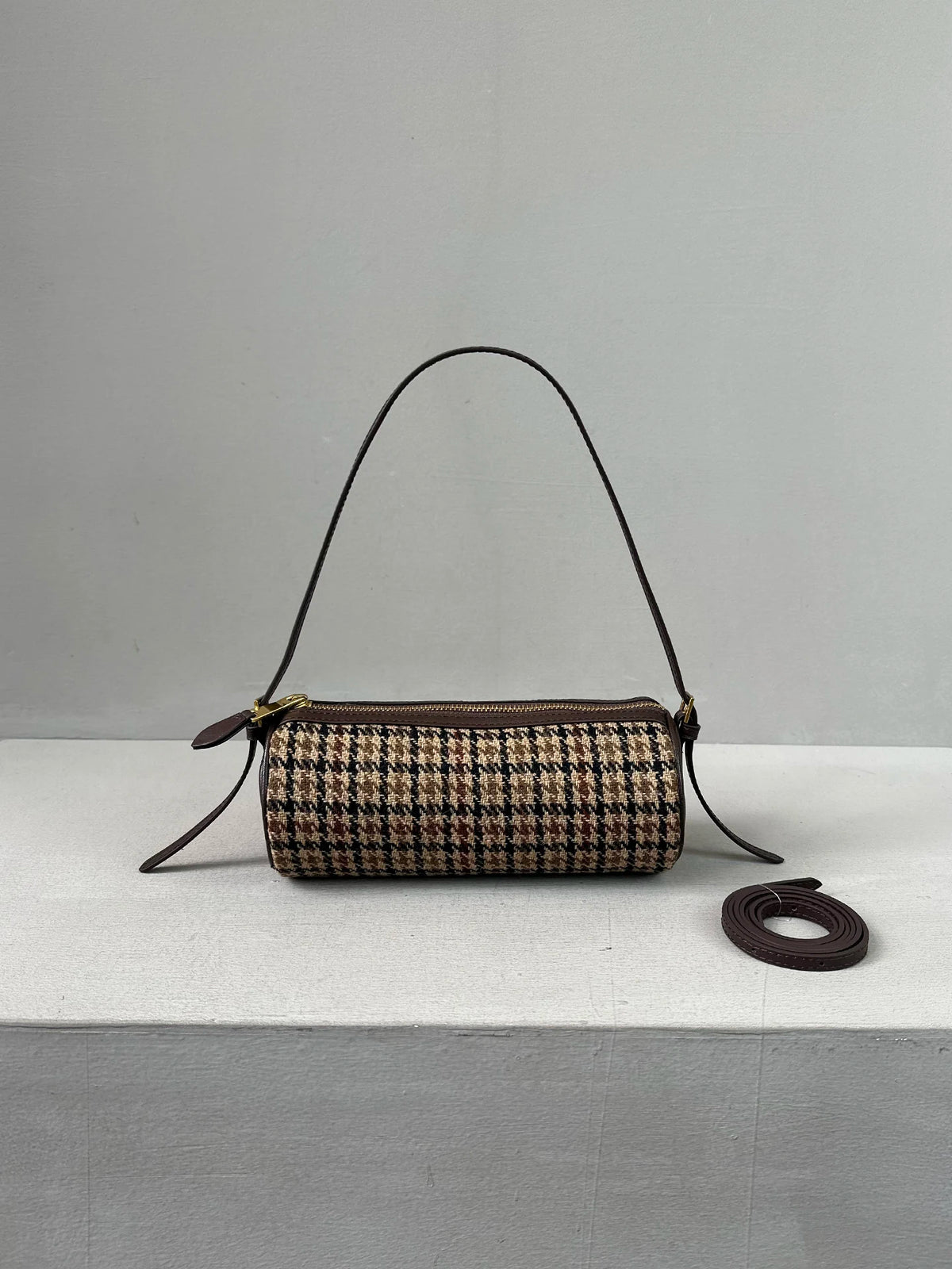 A vintage cow leather cylinder shoulder bag with a brown and black houndstooth pattern displayed on a white surface.