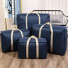 Four navy blue foldable waterproof storage bags with tan straps are displayed on a wooden floor.