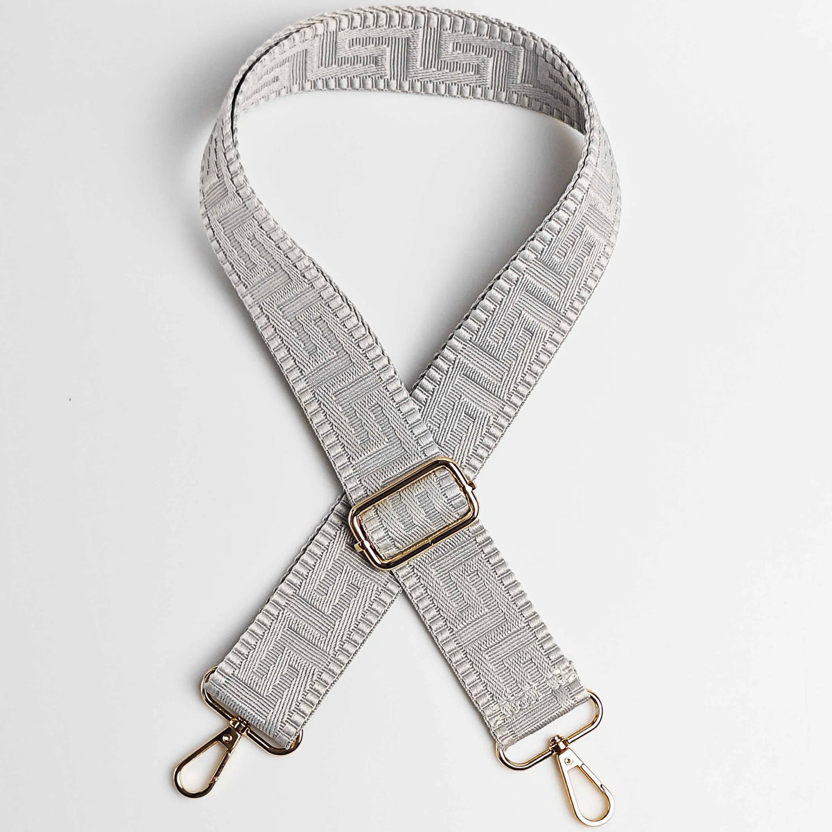 A beige adjustable wide crossbody bag strap featuring a textured maze pattern and gold-toned hardware.