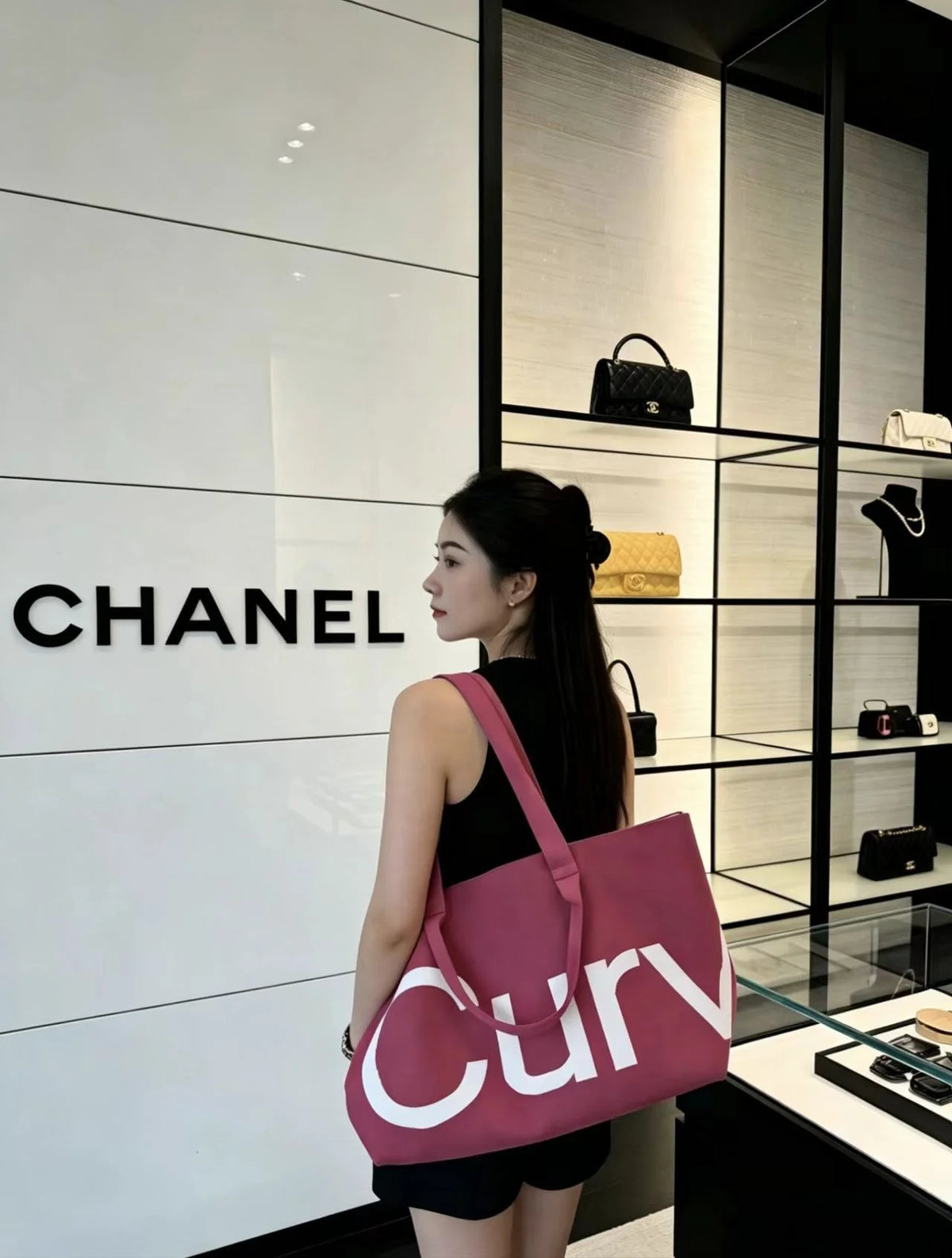 A woman stands in a luxury boutique displaying a pink curved tote bag against a white wall.