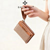 A hand holds a brown leather wallet with a zipper and card slots against a light background.