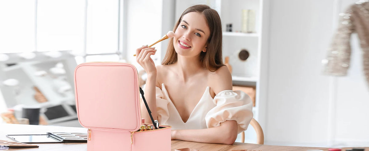 A woman applies makeup using a brush while sitting at a table with a pink LED lighted makeup train case.